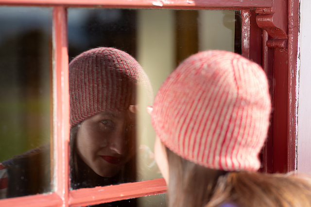 Little Venice mirror 4 balls of yarn in different shades, a hand wearing a knitted handwarmer, knitting needles and a knitted rectangle